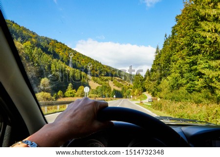 View of the road with a beautiful mountain landscape from the car window in a nice summer or autumn day. Woman's hand on the steering wheel. Female driver seeing beautiful landscape during travel