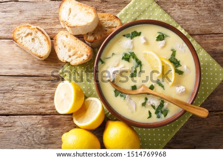 Hot greek lemon soup with chicken close-up in a bowl with bread on the table. Horizontal top view from above
