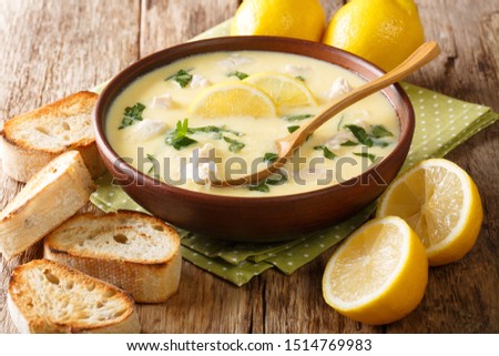Classic Mediterranean lemon soup with chicken close-up in a bowl with bread on the table. horizontal
