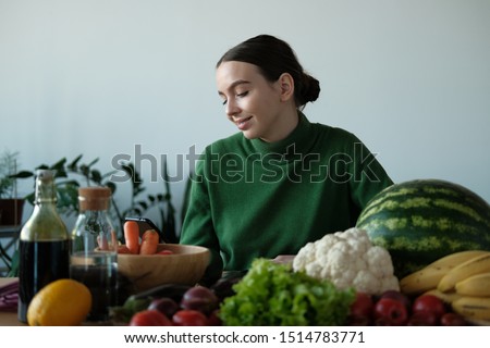 A young girl in a green sweater and Christmas hat is looking for a recipe for cooking on a background of vegetables and fruits. The concept of Christmas and healthy eating.