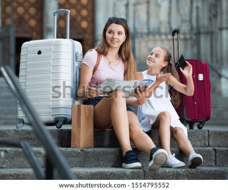 Smiling young mother looking map while daughter photographing sights during joint travel