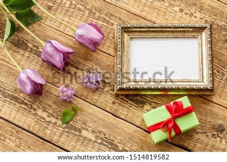 Vintage photo frame with copy space, lilac tulips and gift box on old wooden boards. Top view.