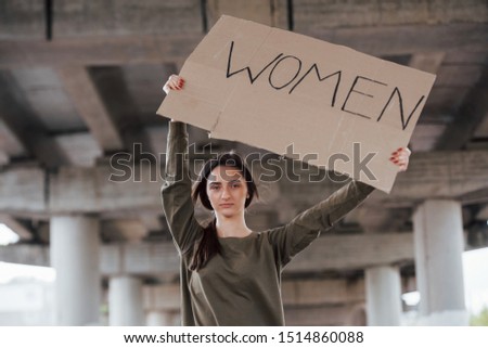 Alone in the area. Pretty girl in casual clothes stands with handmade feminist poster in hands.