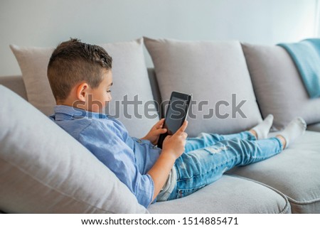 Little boy reading an ebook. Growing up in a technology-based world. Little boy using digital tablet. Little boy with digital tablet sitting on sofa, on home interior background