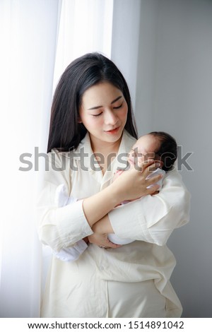 Asian young mother is carrying a newborn lovely baby in white bed room. Duty of the wife to raise children. Mother and child concept. Royalty-Free Stock Photo #1514891042