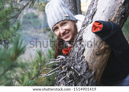 Cheerful girl in a knitted hat near an old tree in the autumn forest.