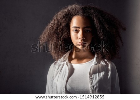 African descent girl wearing white outfit standing isolated on gray background looking camera cool close-up in the dark