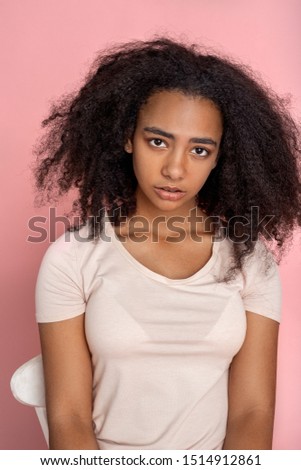 African descent girl sitting on chair isolated on pink background looking camera pensive close-up
