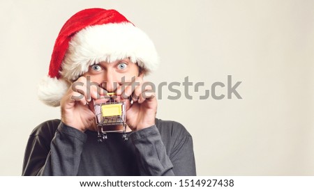 Happy Santa man pushing mini shopping cart. Handsome guy wears Santa hat over white background, copy space. It's time for christmas gifts. Christmas shopping, sales and discounts.