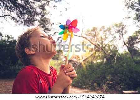 Little handsome boy blows a pinwheel in a forest, carefree, with faded tones and retro style. Royalty-Free Stock Photo #1514949674