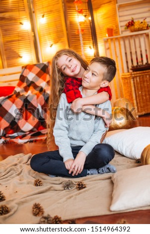 Cute little sister with long hair and an older brother in autumn scenery with pumpkins and plaids play in the studio
