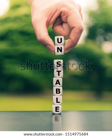 Hand lifts two dice and changes the word "unstable. Royalty-Free Stock Photo #1514975684