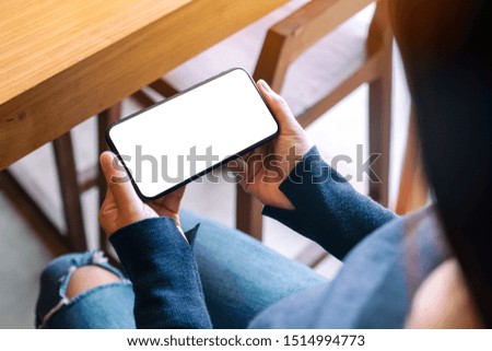 Mockup image of a woman holding black mobile phone with blank white screen in cafe