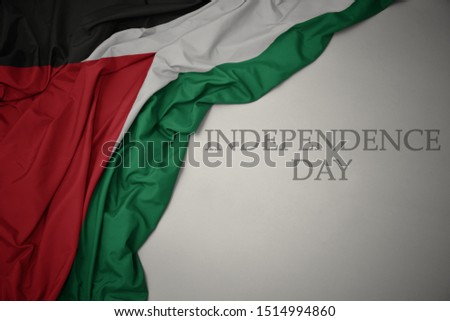 waving colorful national flag of palestine on a gray background with text independence day. concept