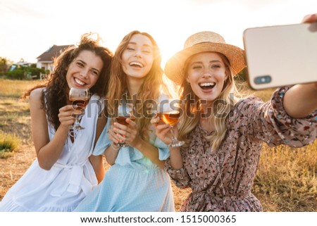 Photo of delighted pretty women taking selfie photo on cellphone while drinking red wine at countryside during sunny day
