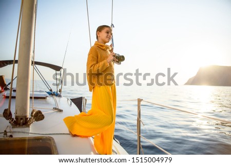 Fashion kid ten years old are posiing on the boat . The happines childhood of freedom. the girl take photo on camera of beautiful view of sunset and nature