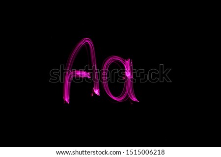 Long exposure photograph of the letter a in capital and lower case, light-painted by fairy lights in neon vibrant pink colour against a black background. Light painting photography.
