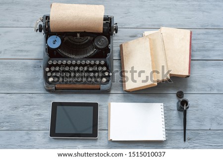 Typewriter, blank page notepad, stack of books and modern digital tablet on gray wooden background.