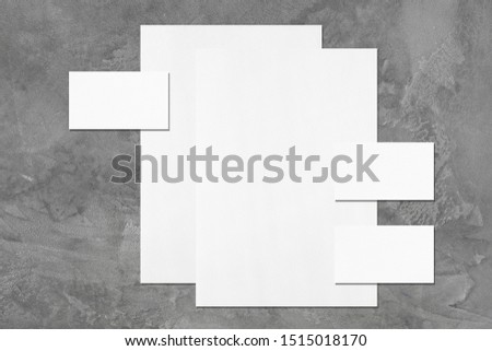 Two empty white vertical a4 sized posters and three horizontal rectangle business card mockups with soft shadows on dark grey concrete background. Flat lay, top view