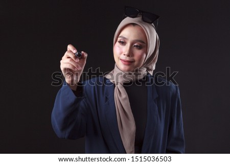 Young muslim business woman writing with black marker on virtual screen, isolated over grey background
