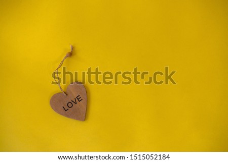 Word "Love" on a wooden figure in the form of a heart lies on a yellow background.