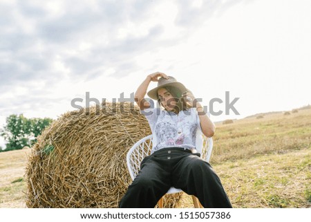 fashion woman in stylish hat sitting happy in sunset at autumn harvest field 