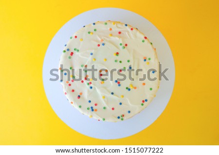 Cake on birthday with colorful rainbow cream on a yellow background decorated with colorful sprinkles, poured with chocolate. Top view.