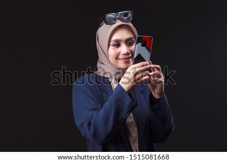 Portrait of young asian muslim businesswoman taking selfie picture using mobile phone while standing isolated on grey background.
