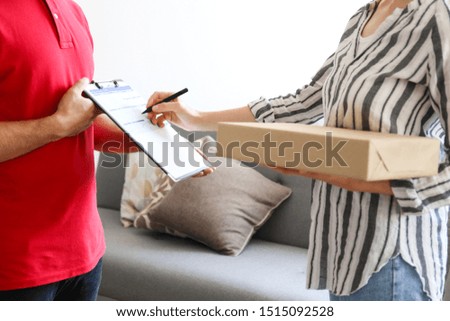 Cropped image of delivery guy in red polo t-shirt handing out the package to young woman. Female receiving the shipment from man wearing shipping company uniform. Background, close up, copy space.