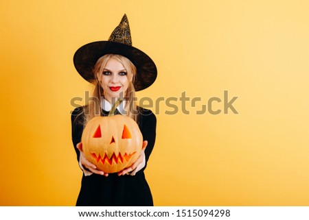 Woman standing against a yellow background  holding pumpkin and showing it on straight hands