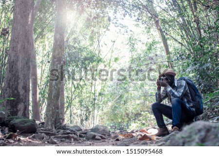 African man traveler carrying backpack and holding camera in the green natural