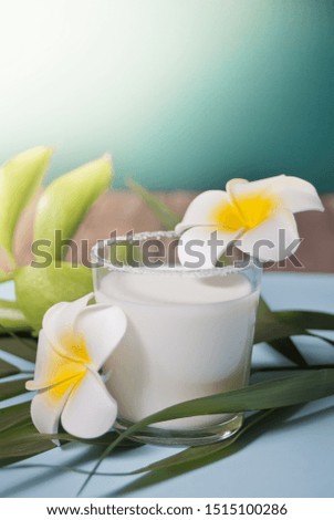 Glass of coconut milk with flowers plumeria and palm leaf