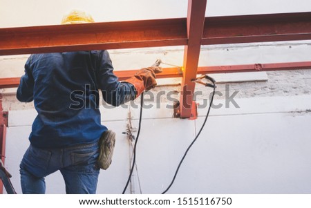 Man welder, protective gloves brews metal welding machine, in the background construction site