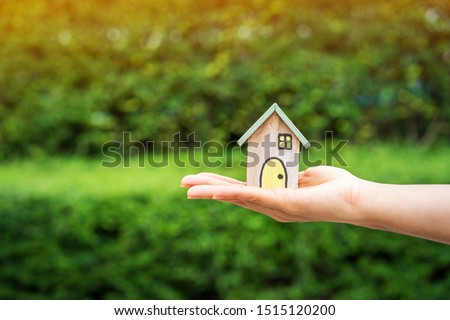 Woman hand holding a wooden home model on the sunlight in the public park, Loan for real estate or save money for buy a new house to family in the future concept.