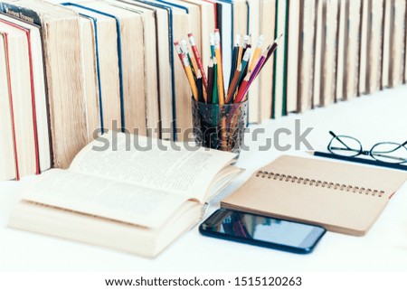 Open textbook, notebook, smartphone, stack of books education back to school background, glasses and pencils in plastic holder with copy space for text