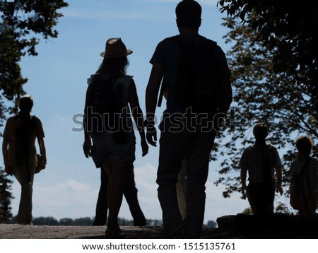 A group of tourists walking in different directions are silhouetted against a blue sky.A lady centre wears a hat which is highlighted. Photographed from low angle. Image