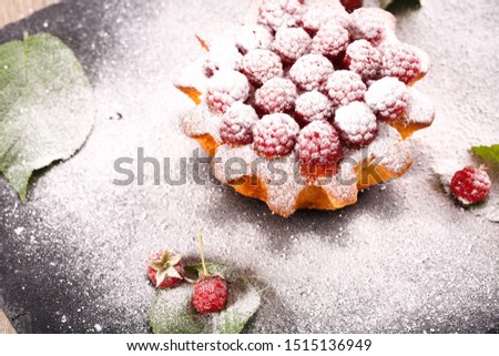 muffin decorated with fresh raspberries on a black plate. All sprinkled with powdered sugar and decorated with green leaves