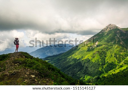 A photographer is taking pictures of one of the mountains of the Aibga Ridge Sochi near Rosa Khutor resort in summer covered with green grass. Sunlights coming through the clouds. 
