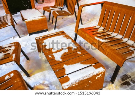 brown wooden table and chairs in the snow, street cafe under the light of a lantern in a winter evening