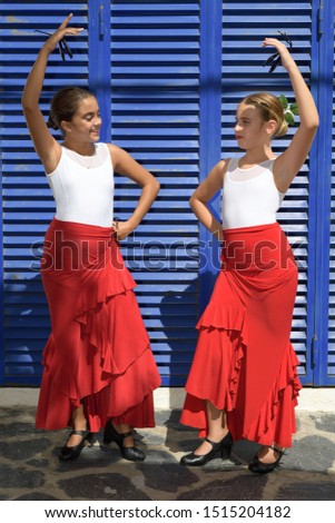Vertical portrait of two girls dancing flamenco. They are in a symmetrical position with the typical handkerchief and looking at each other. It is a sunny day and a typical flamenco scene