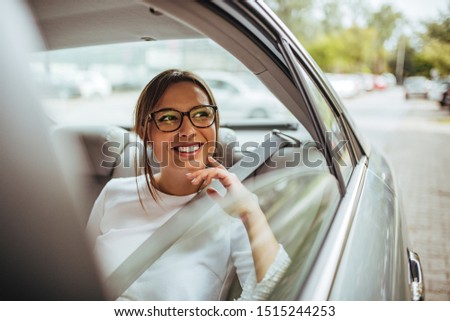 Portrait of a happy young woman in back seat of car looking out of window.