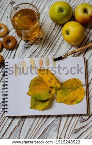 Autumn leaves lay on a drawing pad. on the table is a cup of hot tea