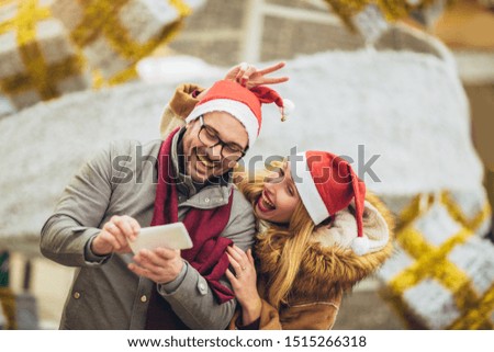 Young beautiful couple with Santa hats make selfie photo in the city.