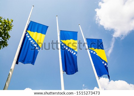 Three bosnian flags in wind on blue sky with clouds Royalty-Free Stock Photo #1515273473