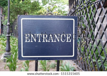 Entrance sign with a background of trees and a gate.