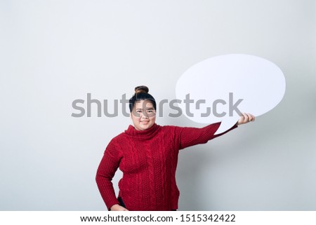 Attractive asian Woman in red sweater holding showing blank speech bubble on light gray background, copy space for text