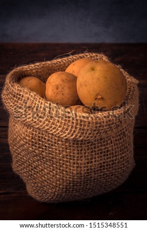 Fresh and raw potatoes in a rustic sack on wooden table