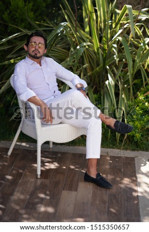 portrait of men in white shirt, white pants and sunglasses sitting on chair