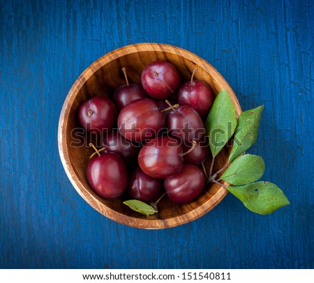 Ripe plums in a wooden bowl on a blue wooden background