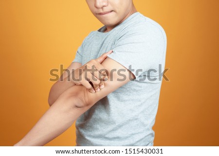 Young Asian man feel hurting his arm. Standing isolated on orange background